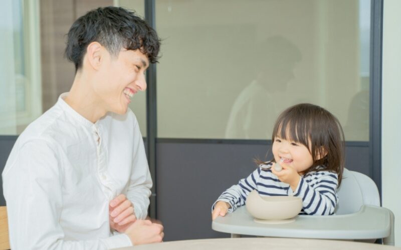 お父さんと女の子の赤ちゃんが笑いながら食事している様子。