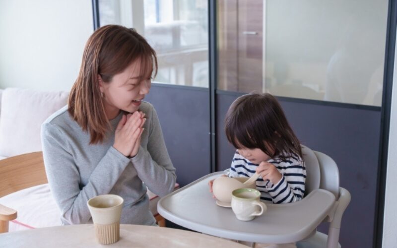 赤ちゃんがスプーンを使って自分で食べる様子を、お母さんが見守っている。