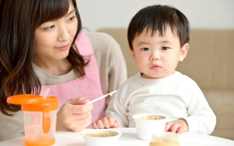 お母さんが離乳食を食べる男の子の様子を見守っている。