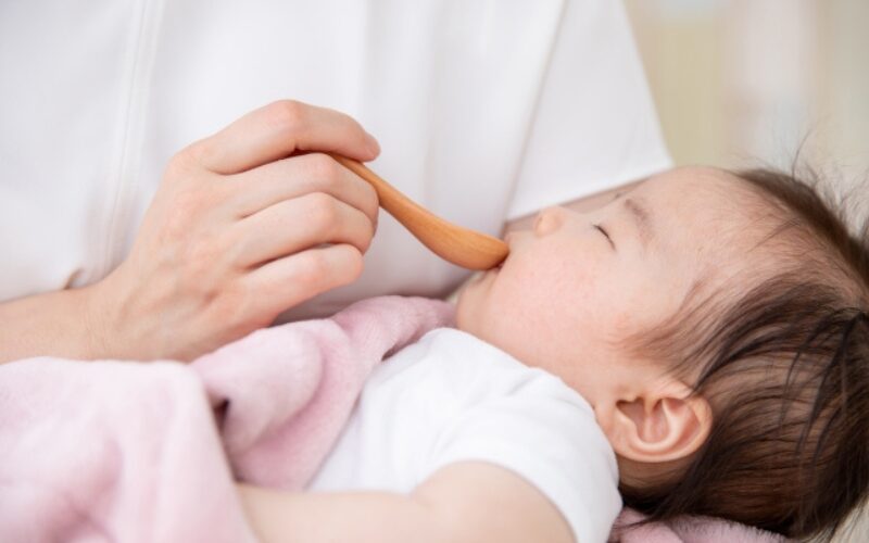 赤ちゃんが抱っこされながら、スプーンで離乳食を食べさせてもらっている。