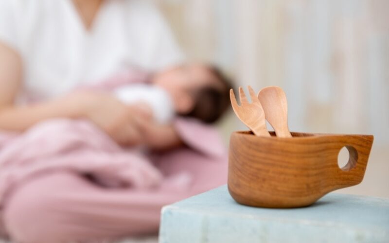 離乳食用スプーンとフォーク。
奥にぼんやり母乳をの飲む赤ちゃんの姿。