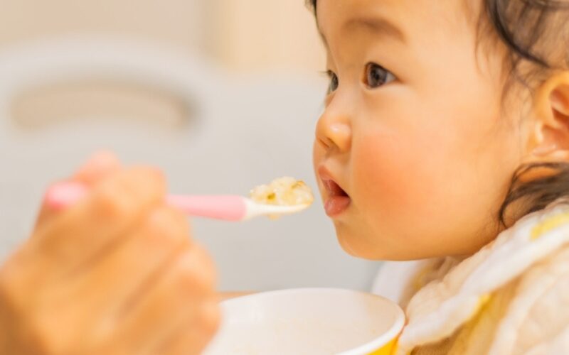 赤ちゃんがスプーンで離乳食を食べさせてもらっている。