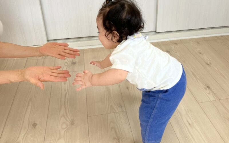 赤ちゃんが大人の手を掴んで、つかまり立ちしようと頑張っている様子。