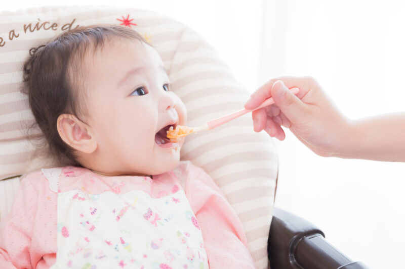 赤ちゃんがスプーンで離乳食を食べさせてもらっている。