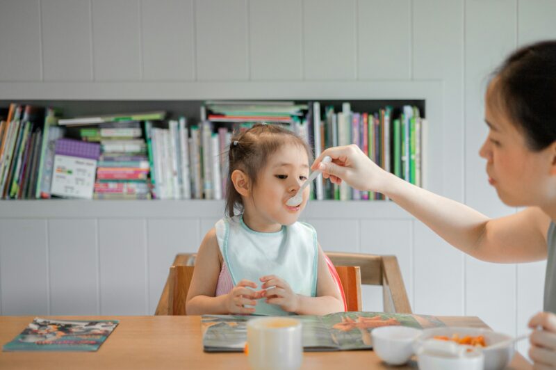 母親がスプーンを使って、赤ちゃんに離乳食を食べさせている。
